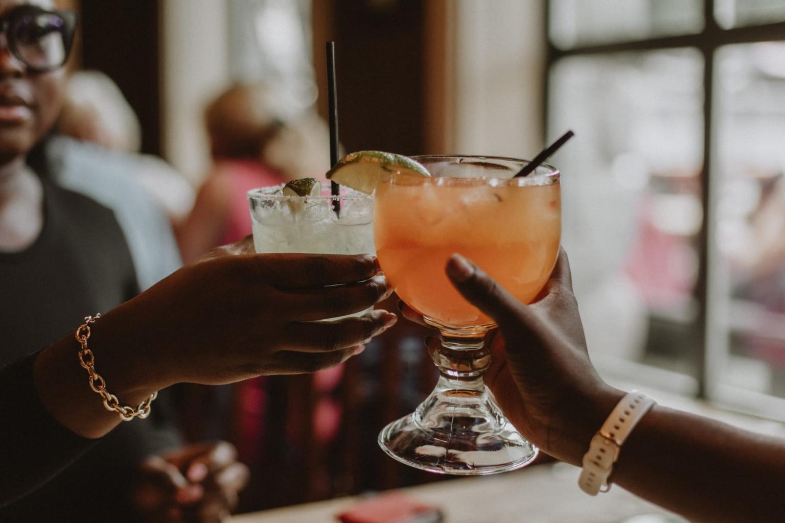 Three people clinking cocktails in a warmly lit room.
