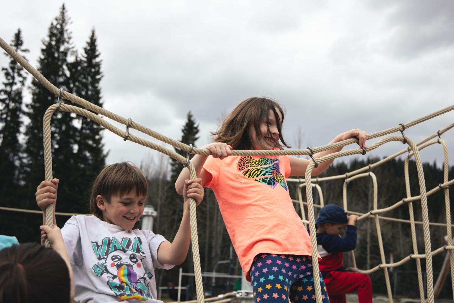 Children climbing a rope net outside on a cloudy day.