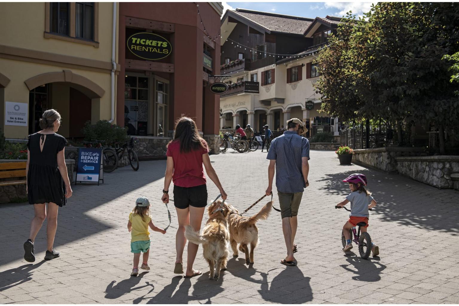 Family walking with dogs and child on a bike in a pedestrian street.