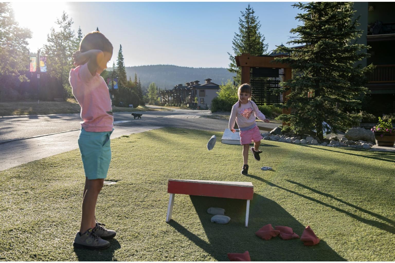 Children playing outdoor bean bag toss in sunny park.