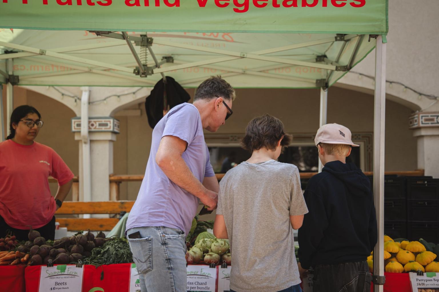 Three people shopping at an outdoor market stall.