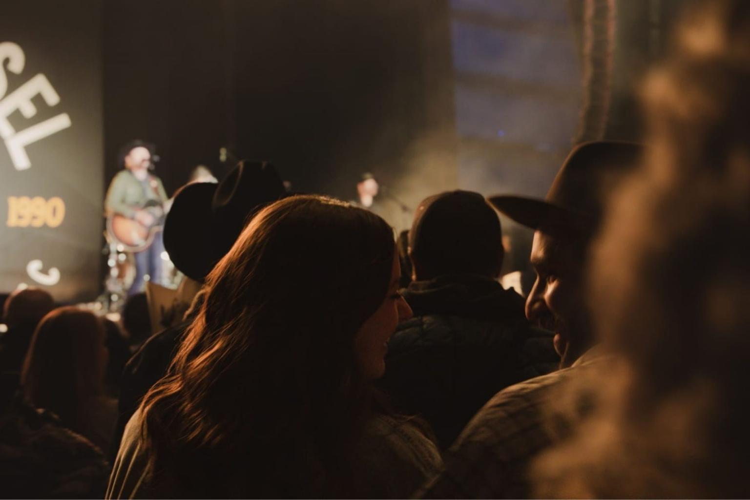 Concert crowd watching a band perform on stage. Dim lighting creates a warm atmosphere.