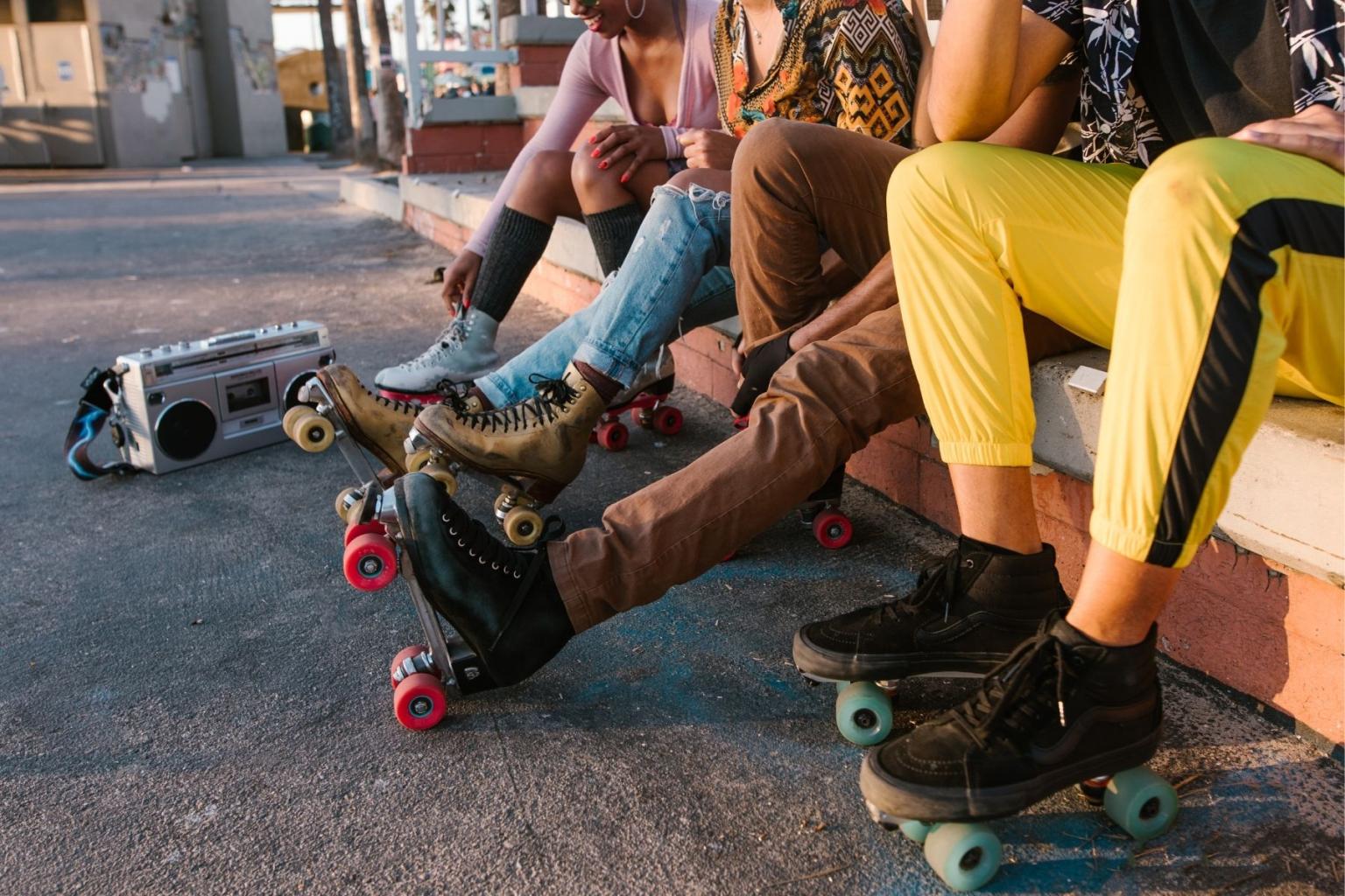 People wearing roller skates sit on a curb beside a boombox.