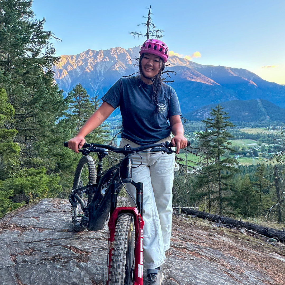 Woman with a bike on a rocky mountain trail, scenic view in background.
