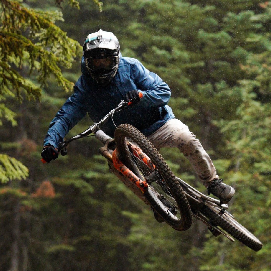Mountain biker jumping in a forest, wearing a helmet and blue jacket.