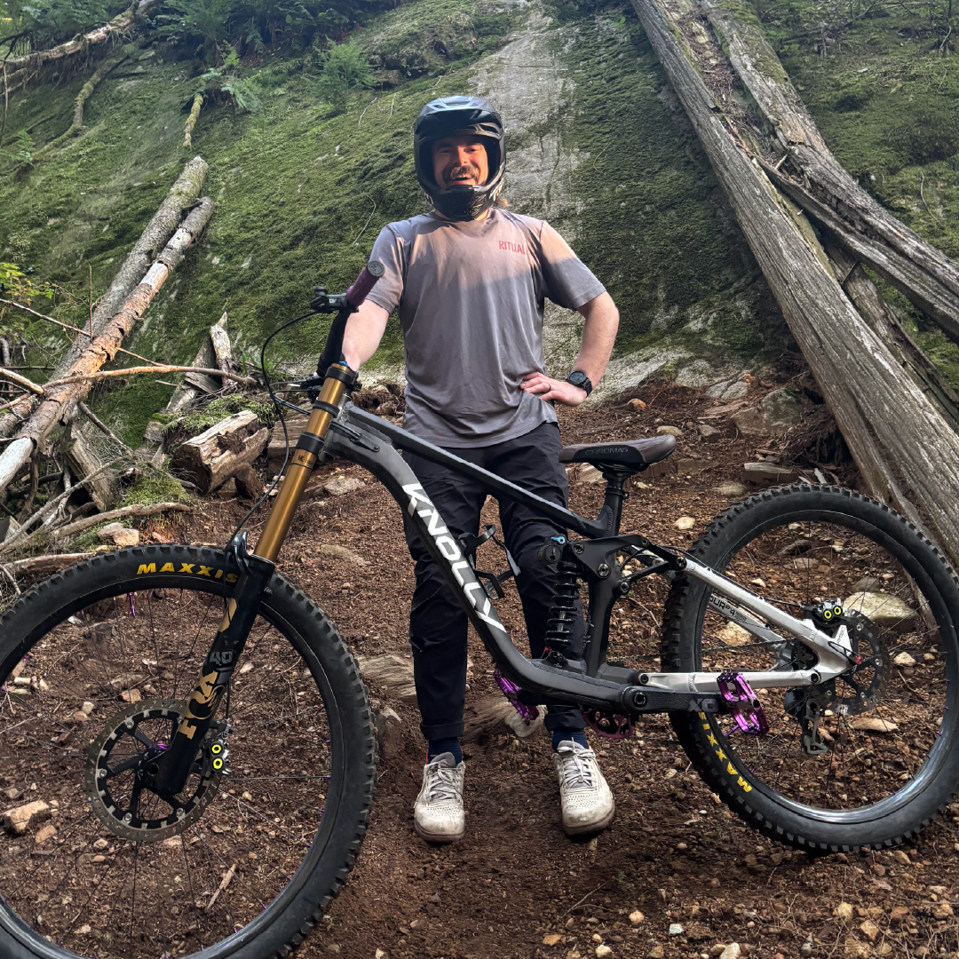 Mountain biker in gear standing beside a bike on a forest trail.