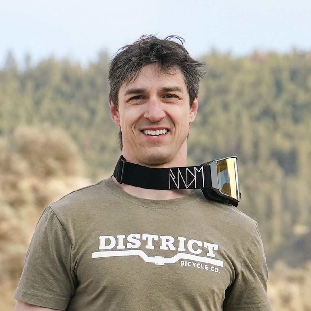 Smiling man outdoors with goggles around neck.