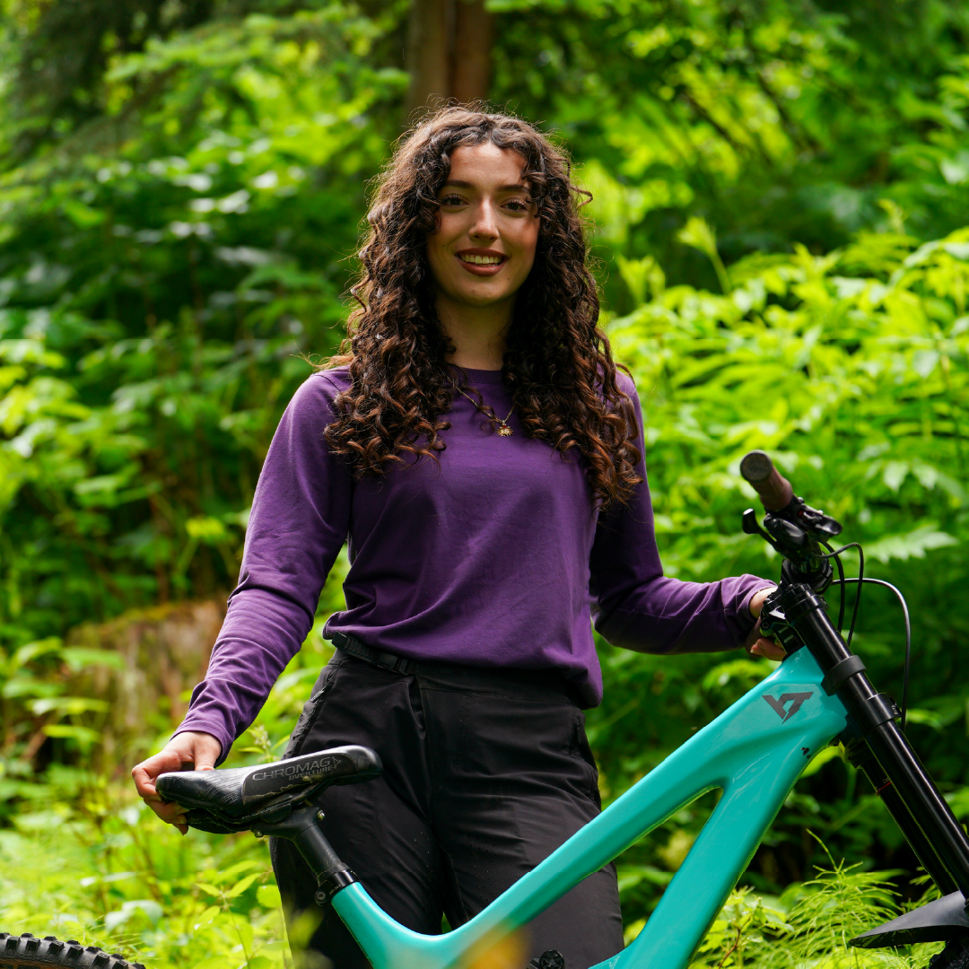 Woman with a bicycle in a lush, green forest.