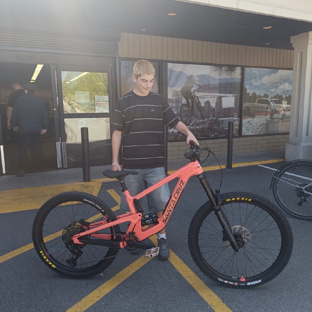 Boy standing with a red mountain bike outside a store.