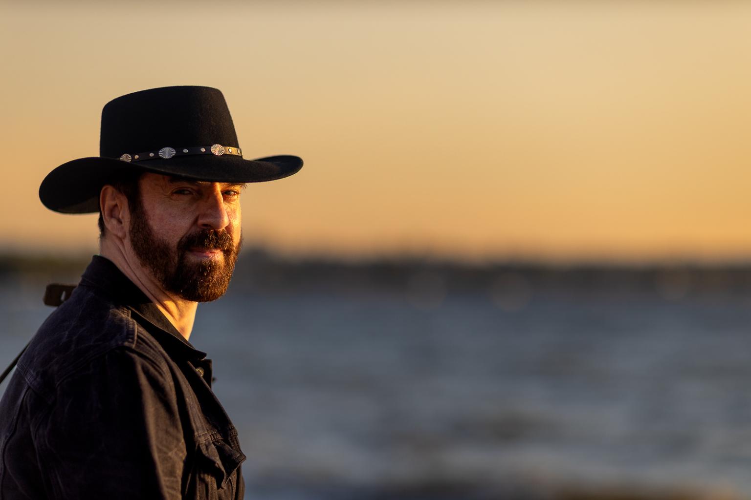 Troy Toma - Man in a hat by the sea at sunset.