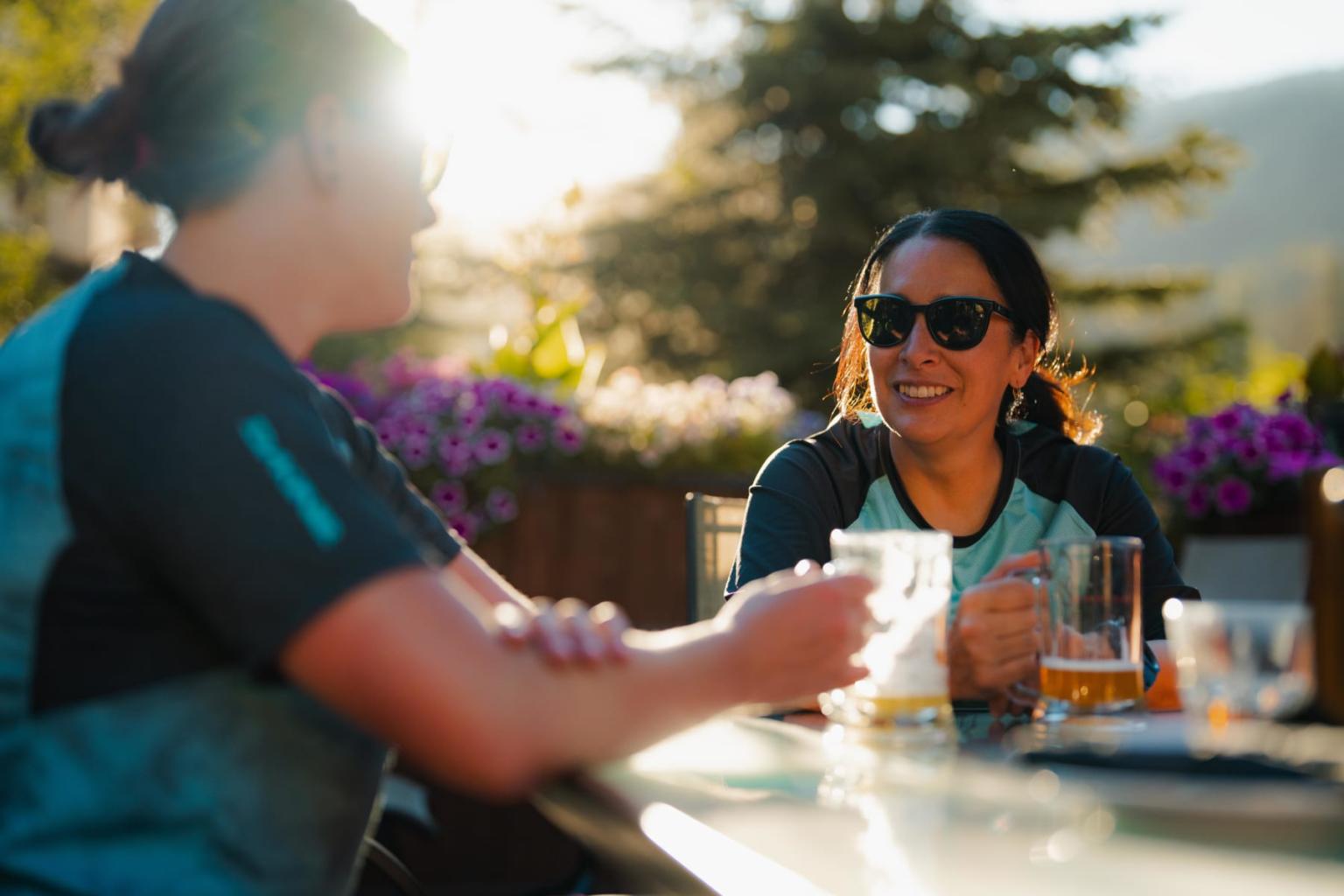 Two people smiling, enjoying drinks outside in sunlight.