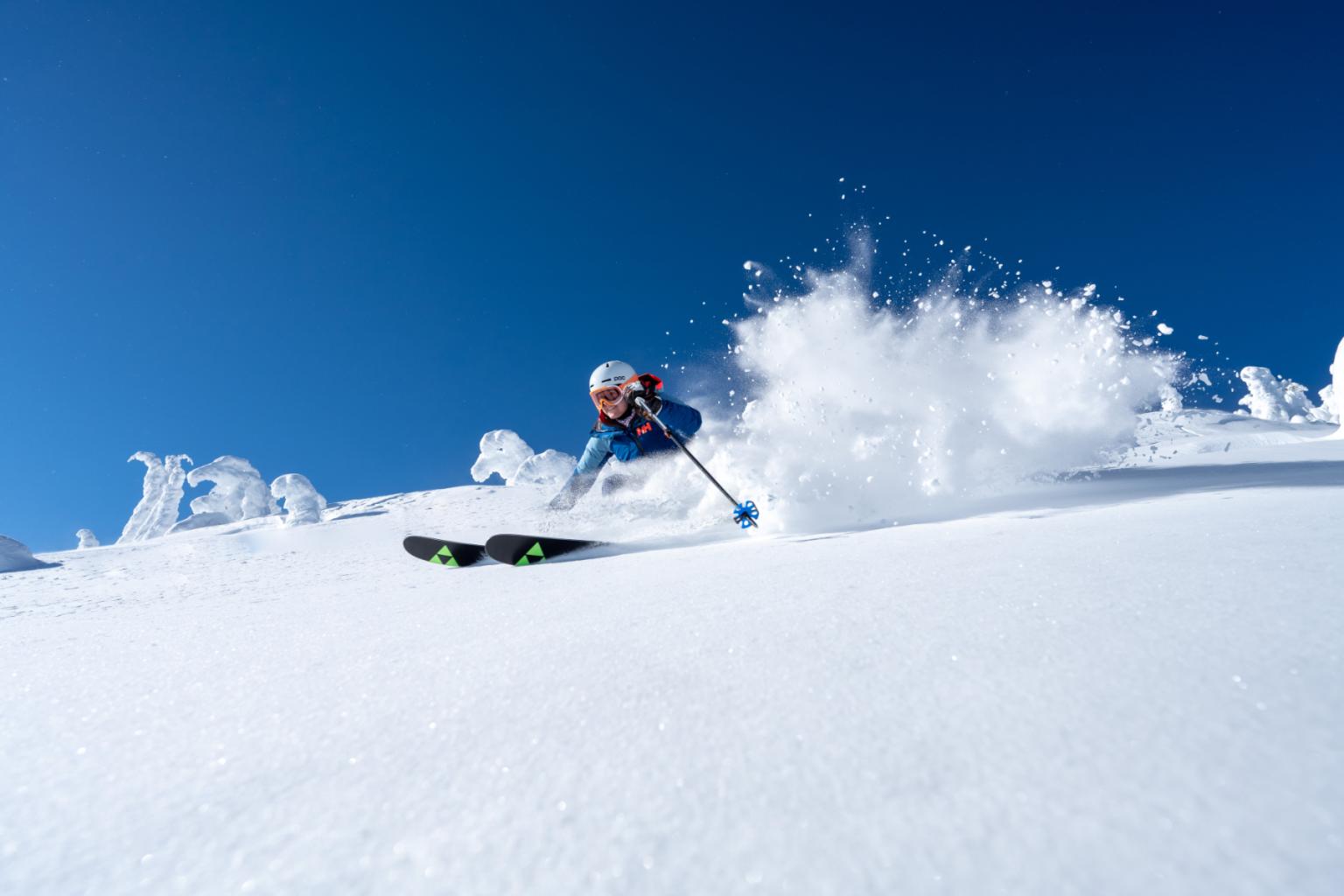 Skier racing down a snowy slope under a clear blue sky.