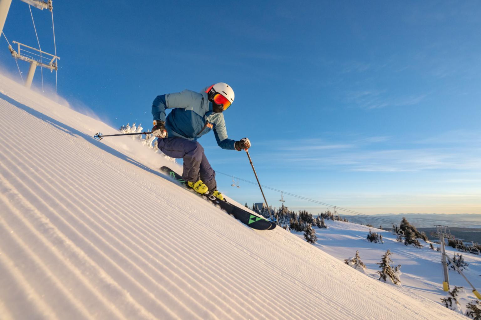 Skier in blue jacket descending a sunlit snowy slope.