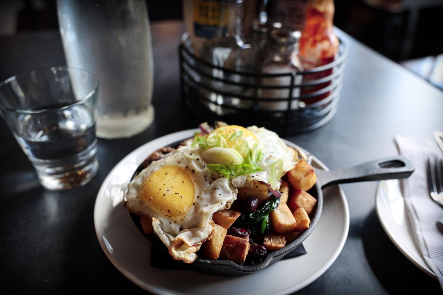 Skillet with eggs, potatoes, and veggies on a plate, with a water glass nearby.