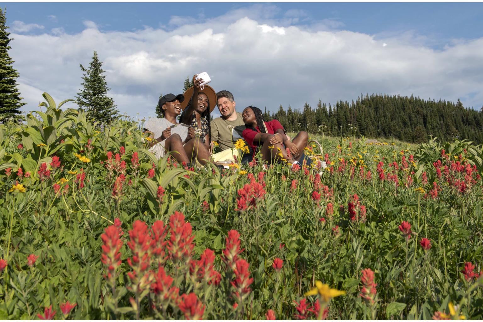 Group sitting in a colorful meadow, smiling under a partly cloudy sky.