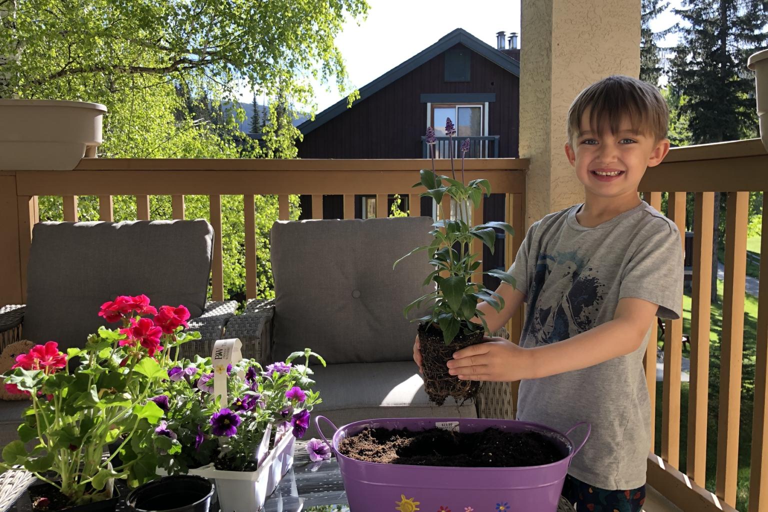 Young boy smiling, planting a seedling on a sunny porch.