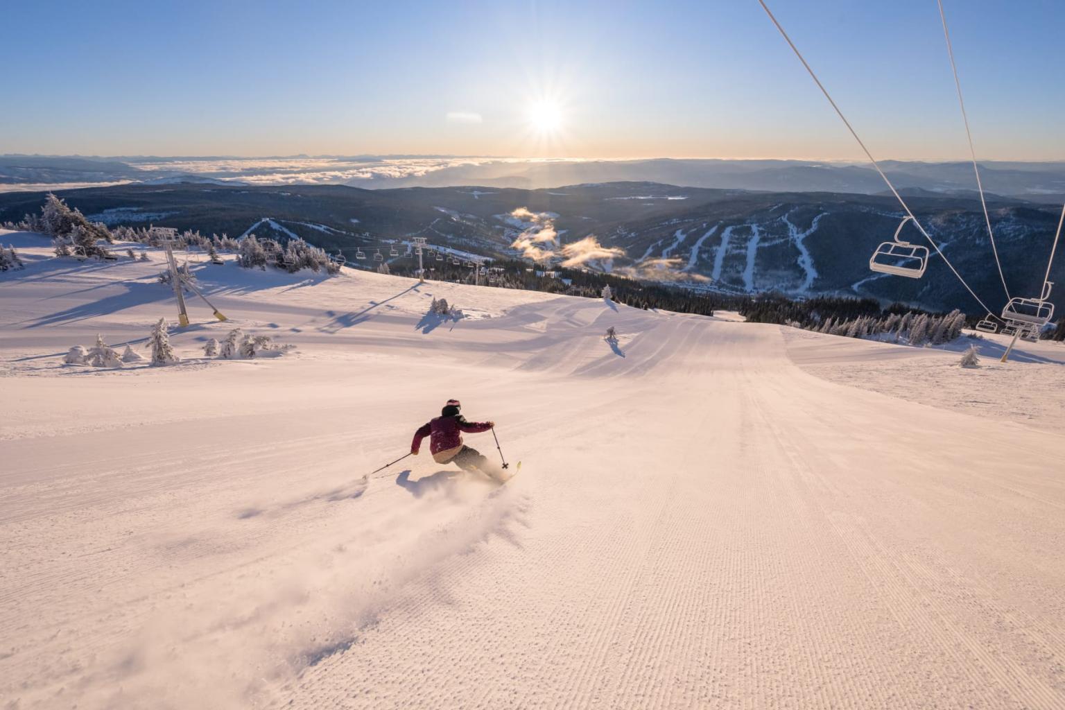 Skier on a sunlit snowy slope, distant mountains in view.