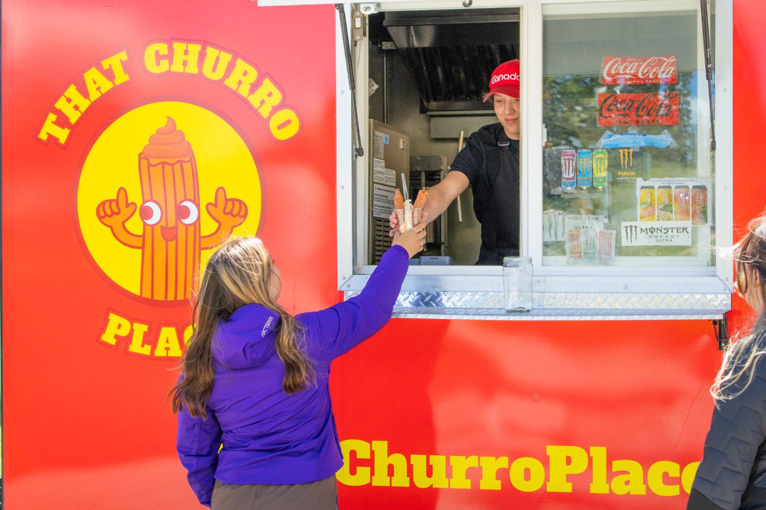 Red food truck serving a churro to a customer.