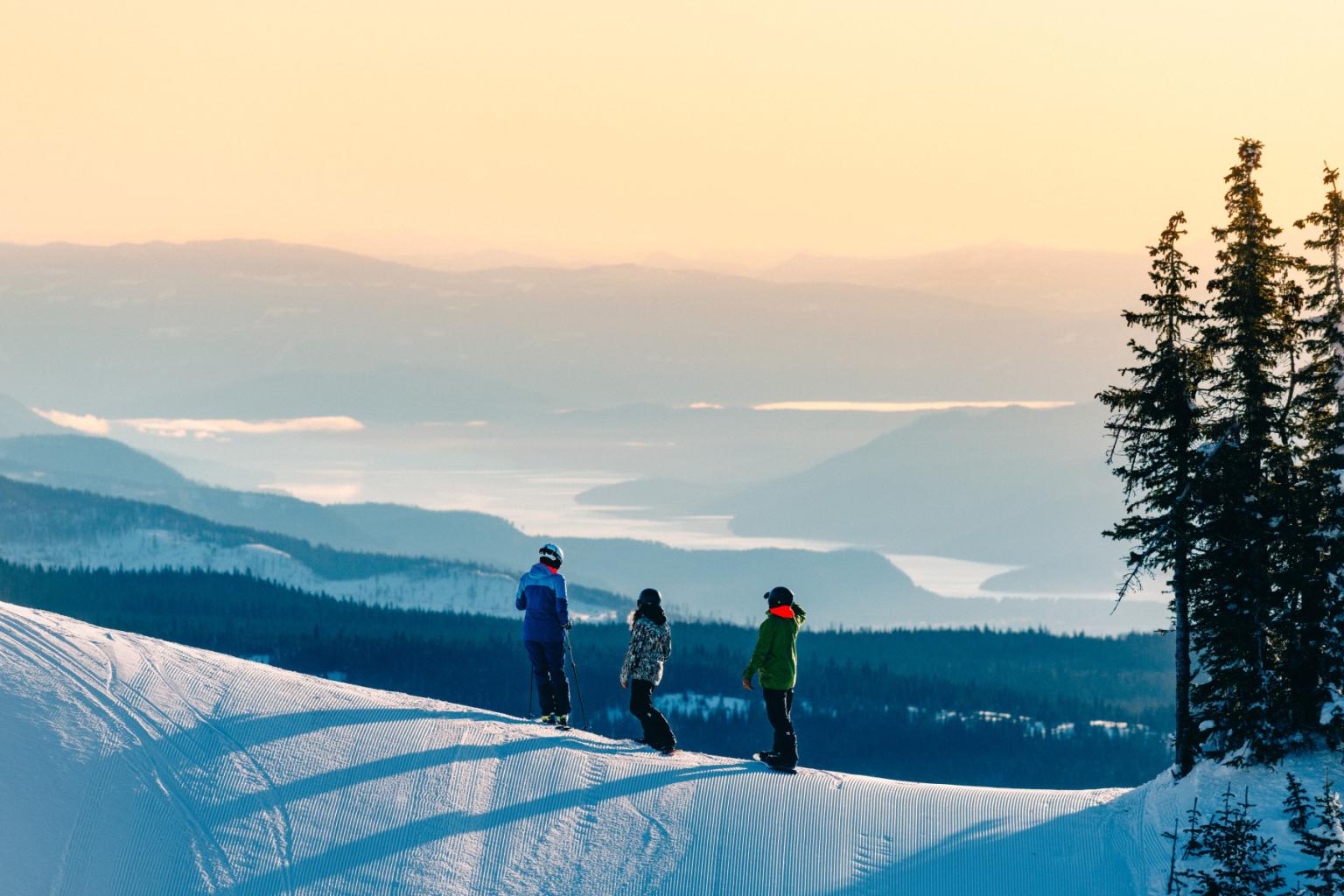 Skiers standing on snowy slope with scenic mountain view at sunset.