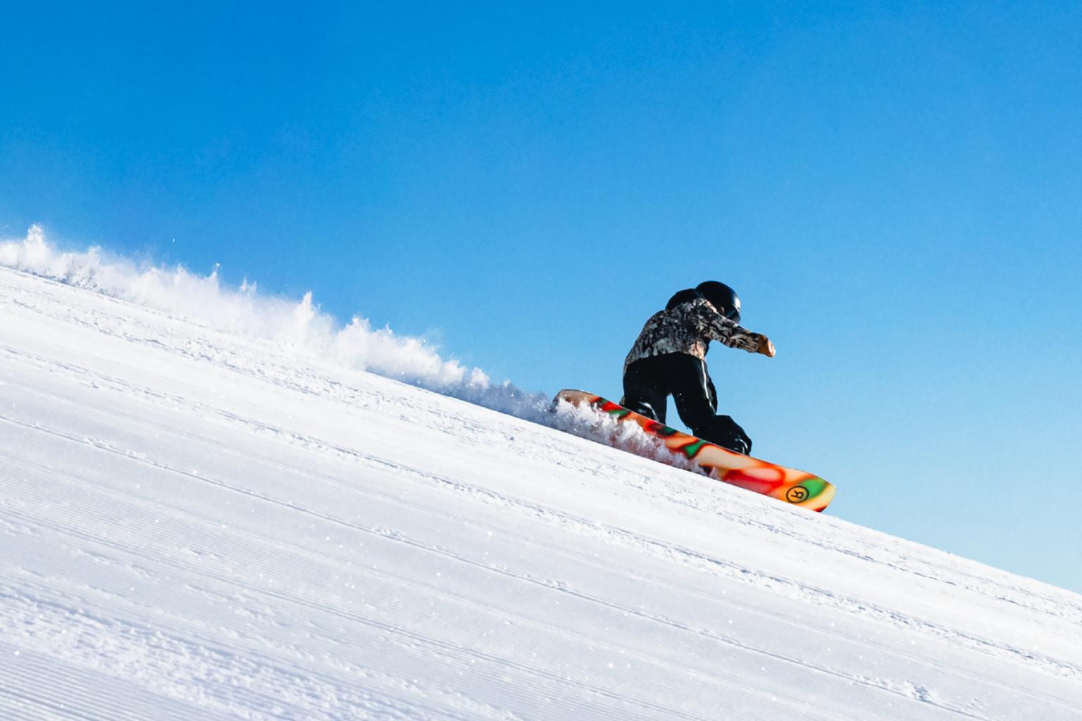 Snowboarder gliding down a snowy slope under a clear blue sky.