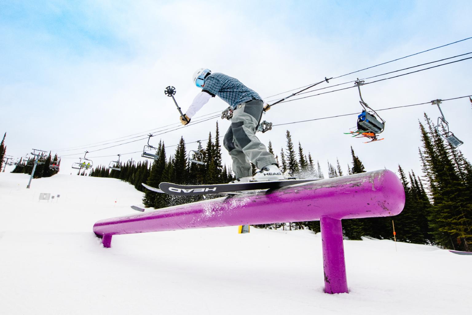 Skier in grey outfit sliding on a purple rail in a snowy area.