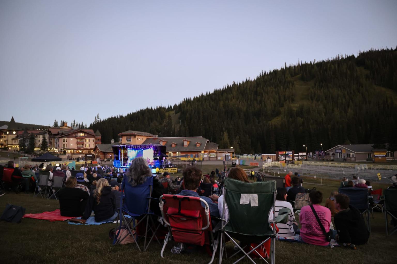 Outdoor crowd watching a show at dusk, with mountains in the background.