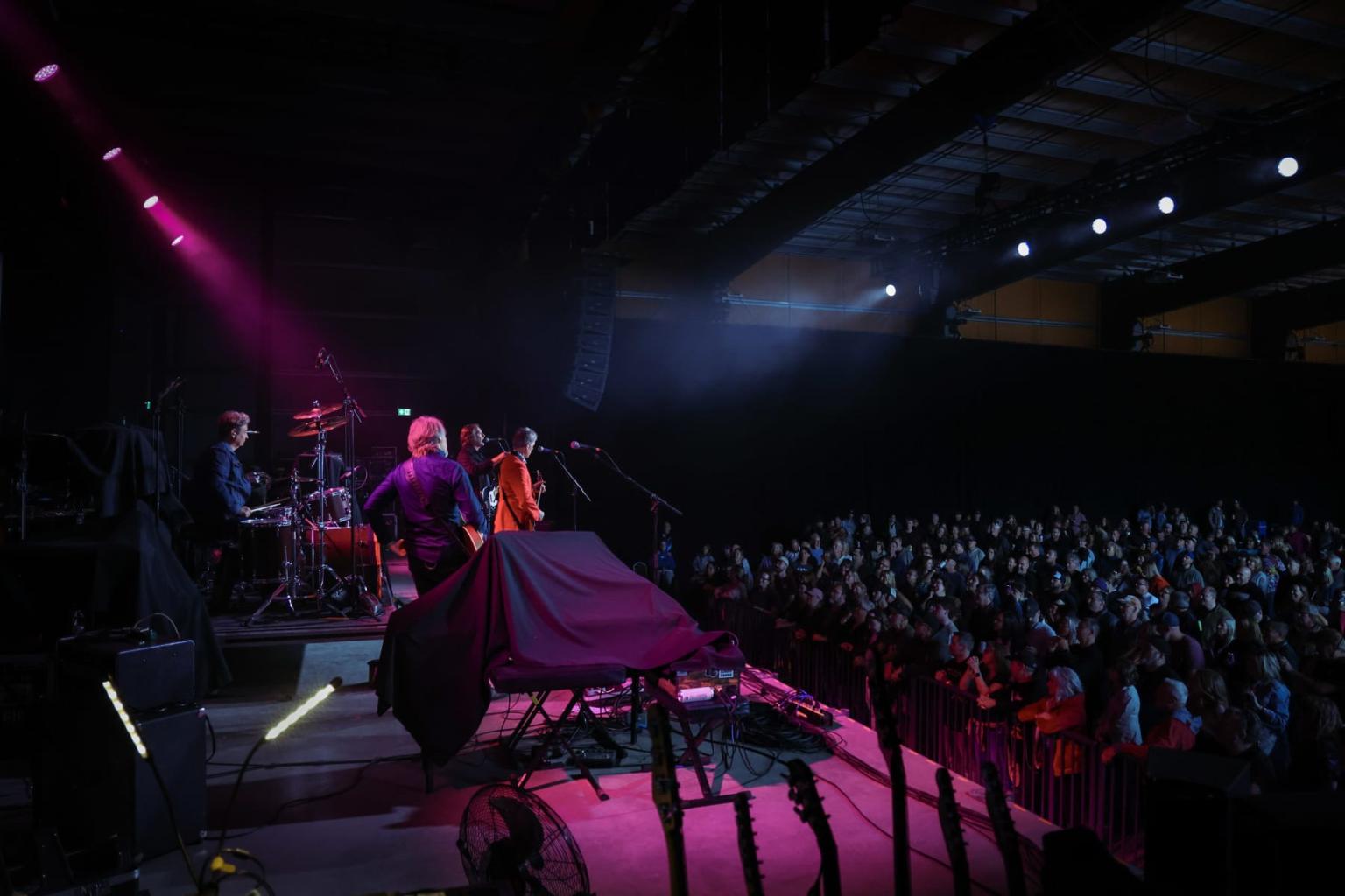Concert stage with a band under purple lights, audience in the foreground.