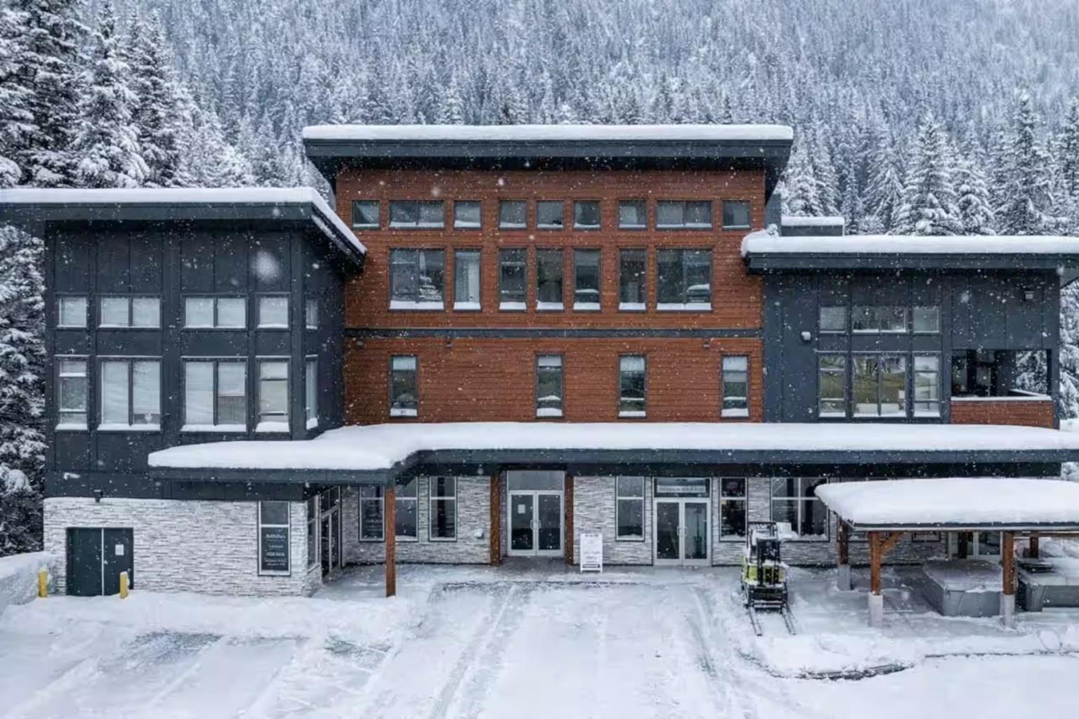 Snow-covered building surrounded by trees, with a mountain backdrop.