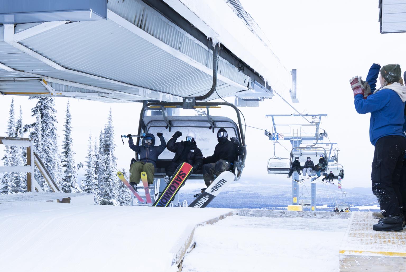 Skiers on chairlift reaching snowy mountain top, with a snowy backdrop.
