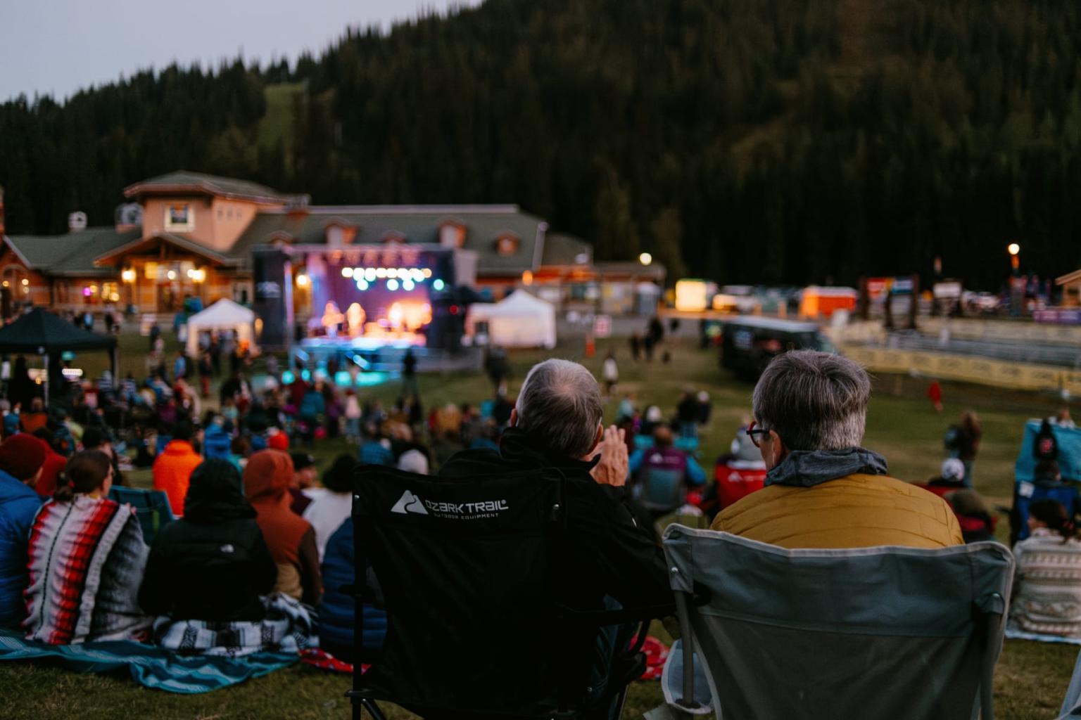 Outdoor concert at dusk with a crowd on a grassy hill.