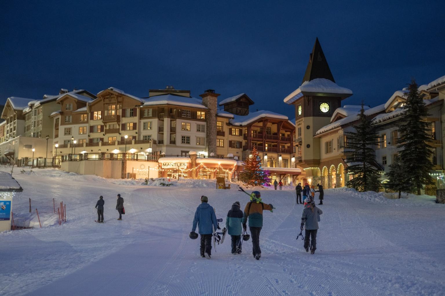 Nighttime skiers on a snowy slope below illuminated alpine hotels.