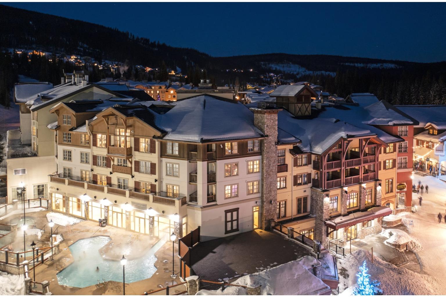 Snow-covered alpine village at dusk, with warmly lit hotels and streets.
