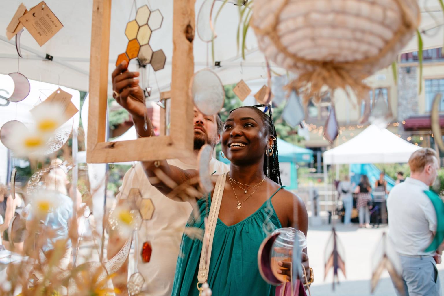 Smiling woman in green dress shopping among hanging crafts at an outdoor market