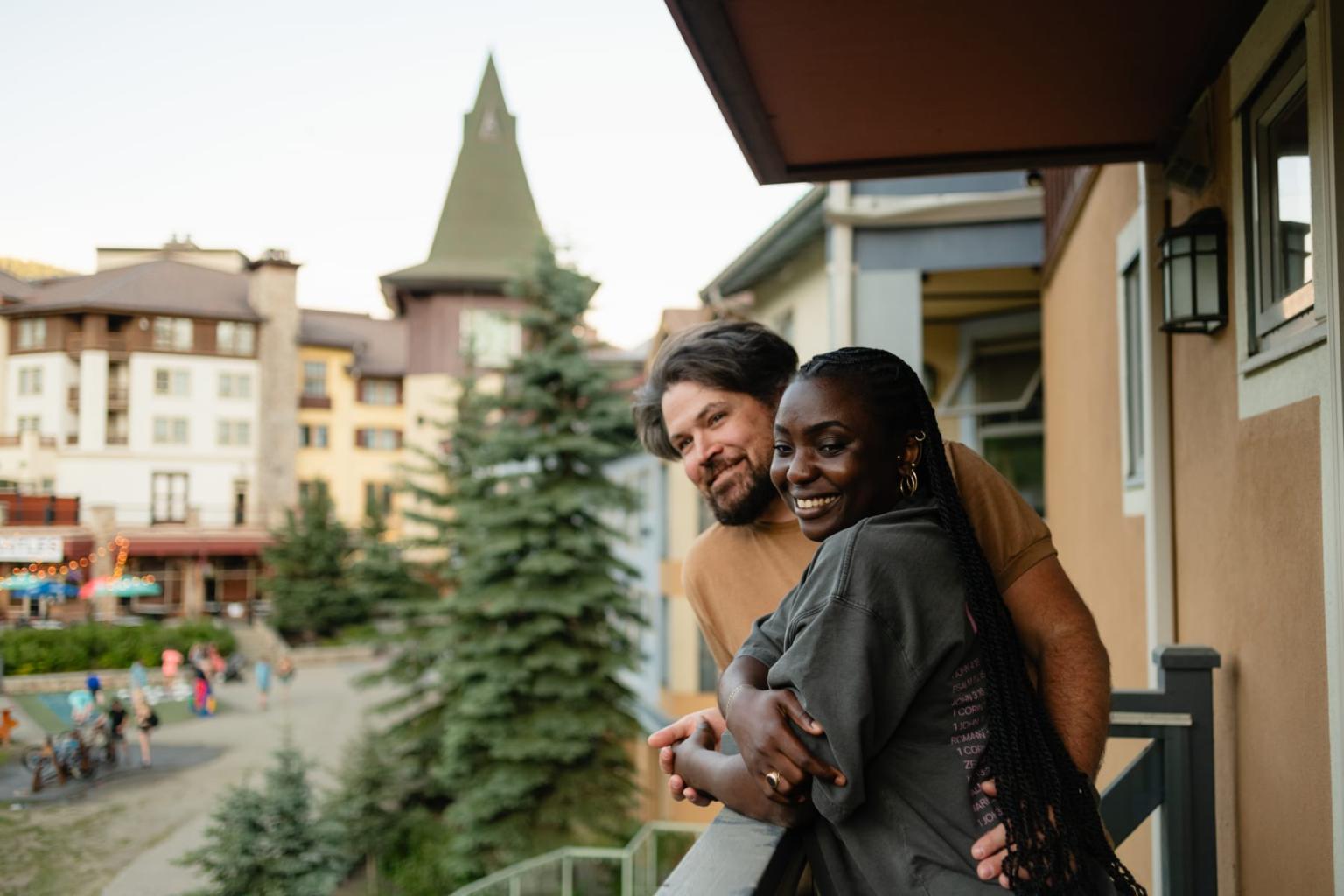 Smiling couple embracing on a balcony overlooking a town square.
