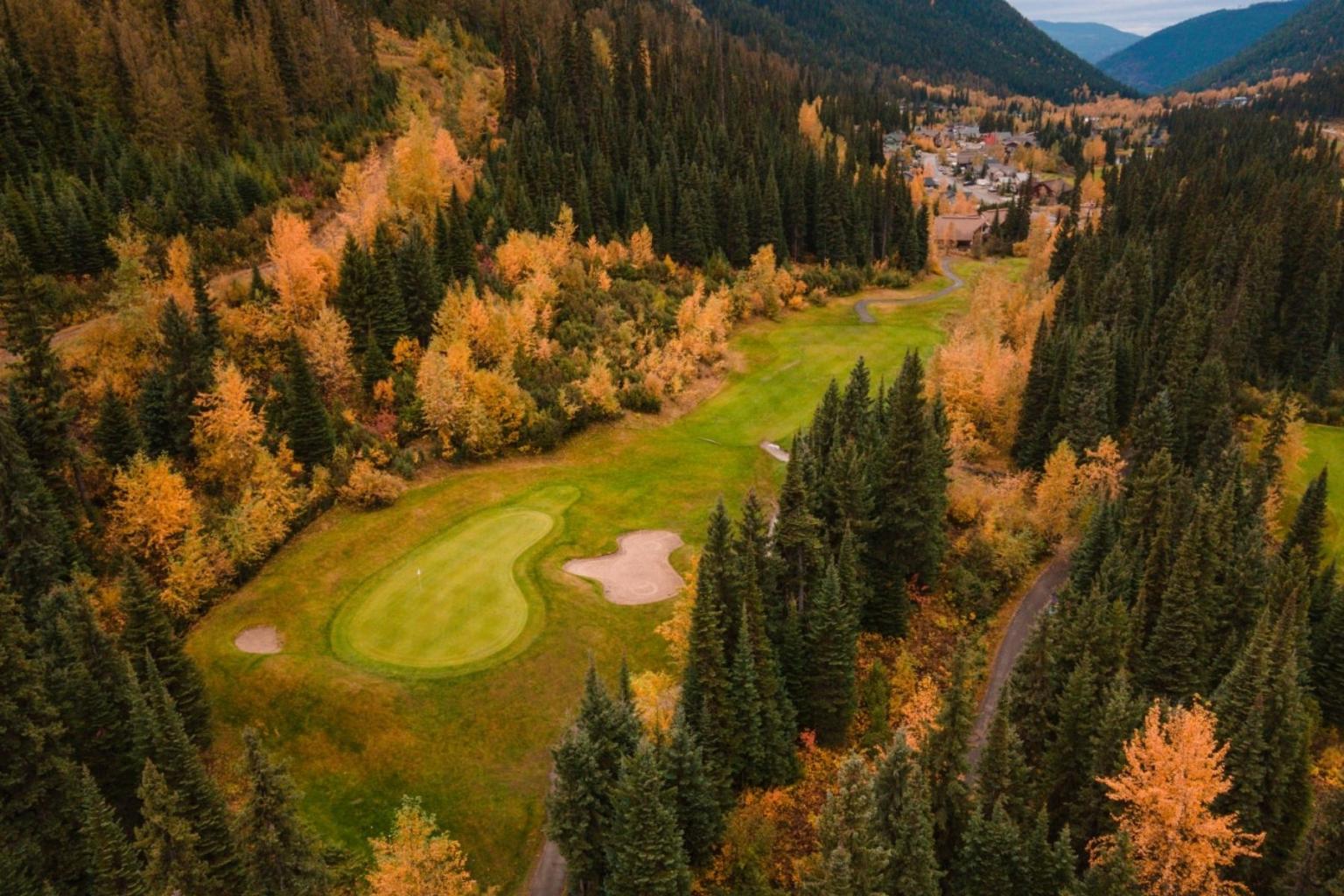 Aerial view of a green golf course amid autumn forested mountains.