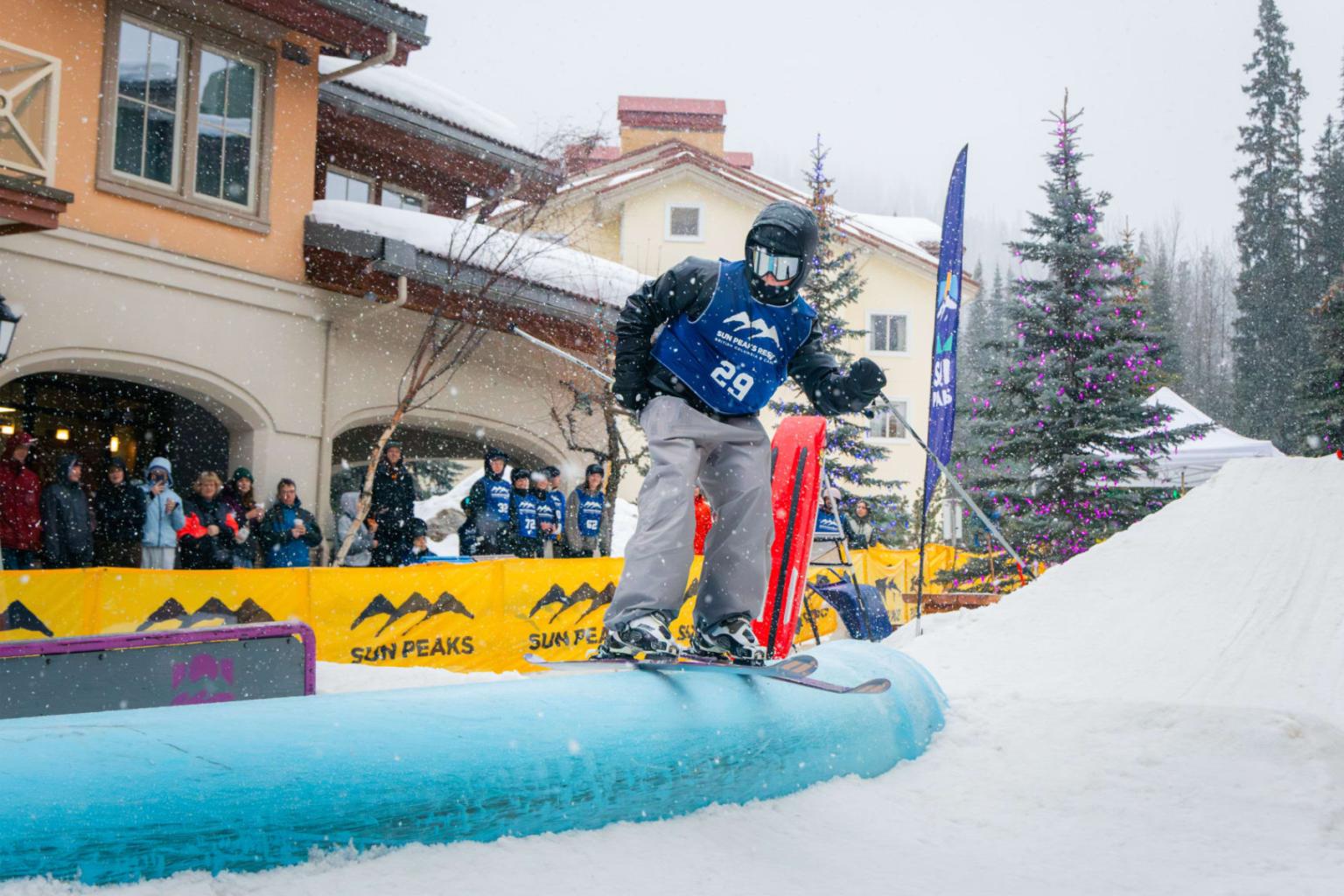 Snowboarder jumping over a blue rail at a snowy ski resort.