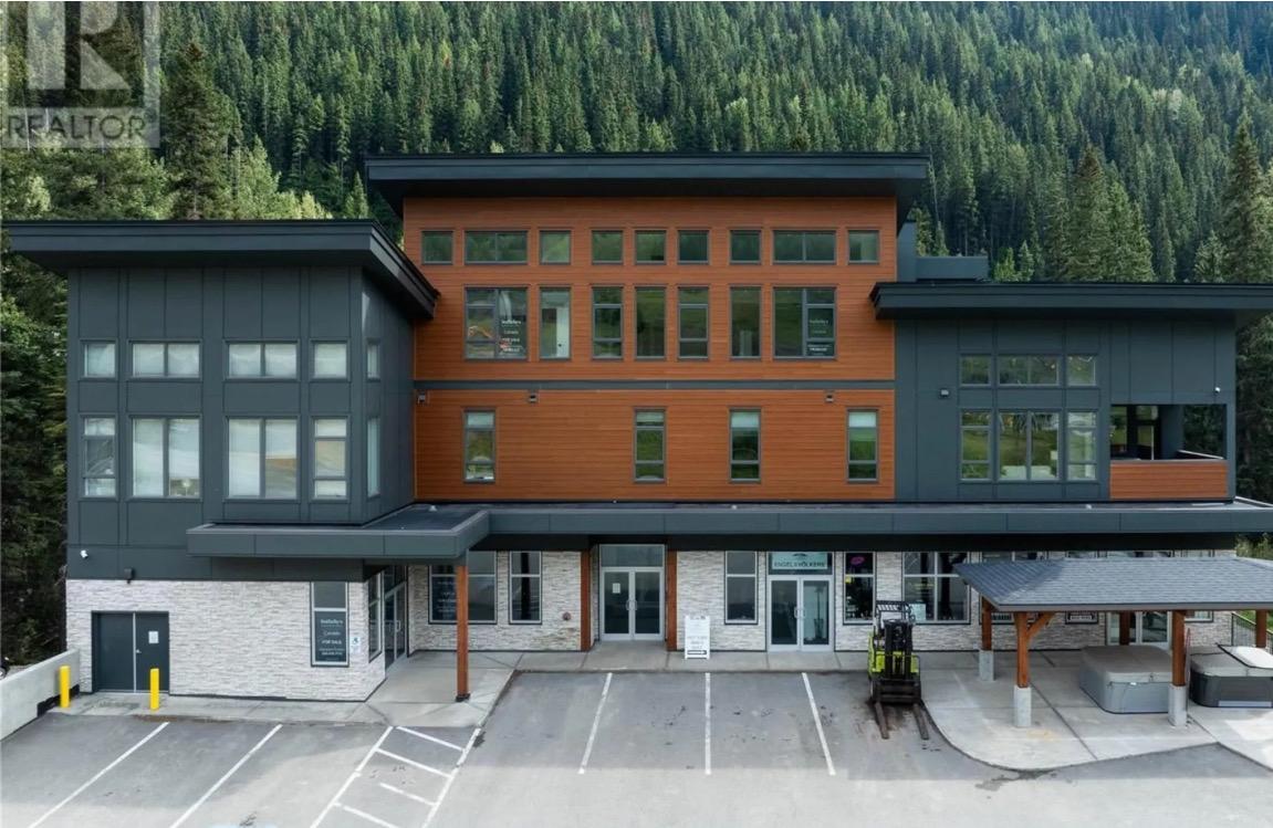 Modern wood-and-glass building beside a forested hillside.