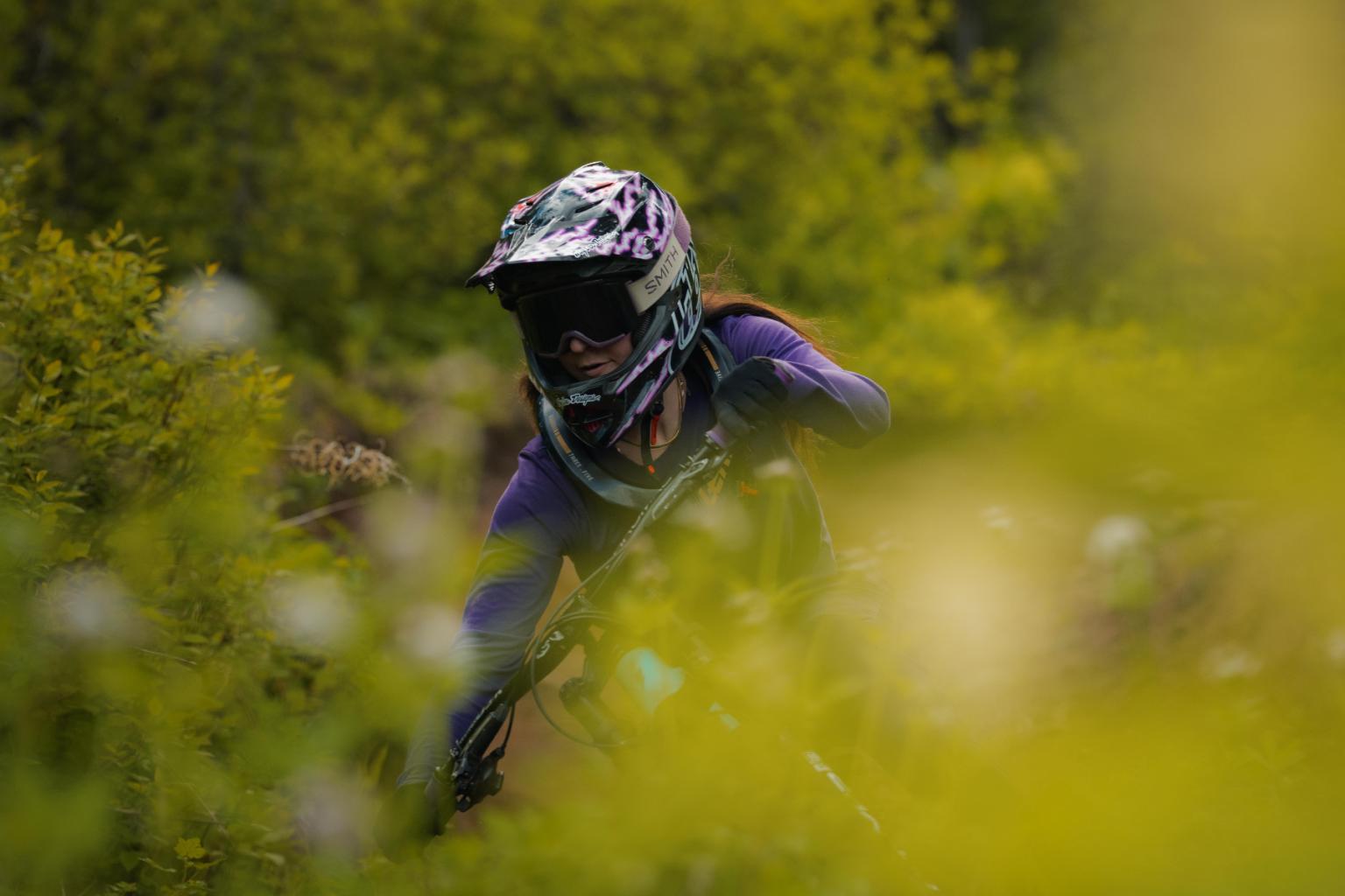 Mountain biker in helmet riding through blurred green foliage.