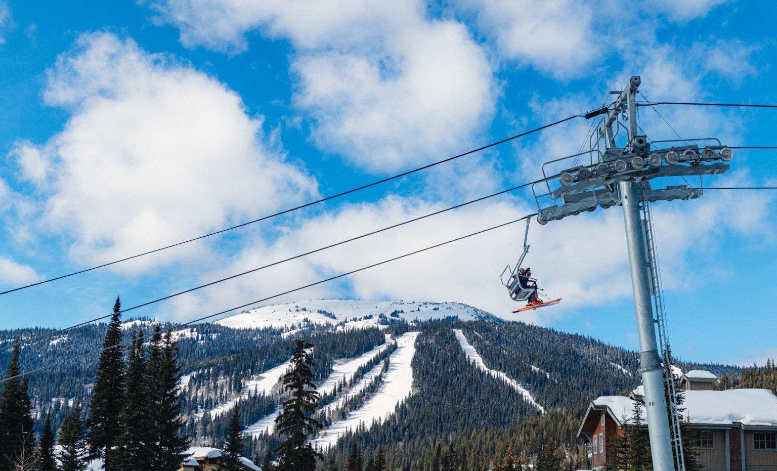 skiers on a chairlift in foreground waving with sun peaks tod mountain in background