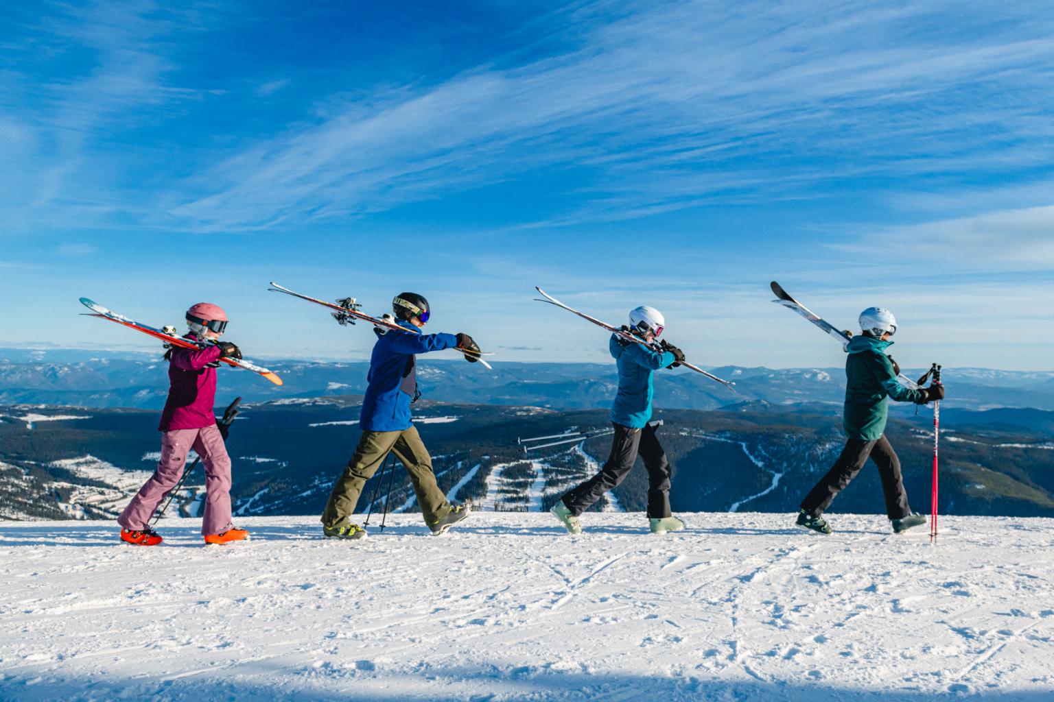 Four skiers walking in a line with skis over shoulders in the Sun Peaks alpine