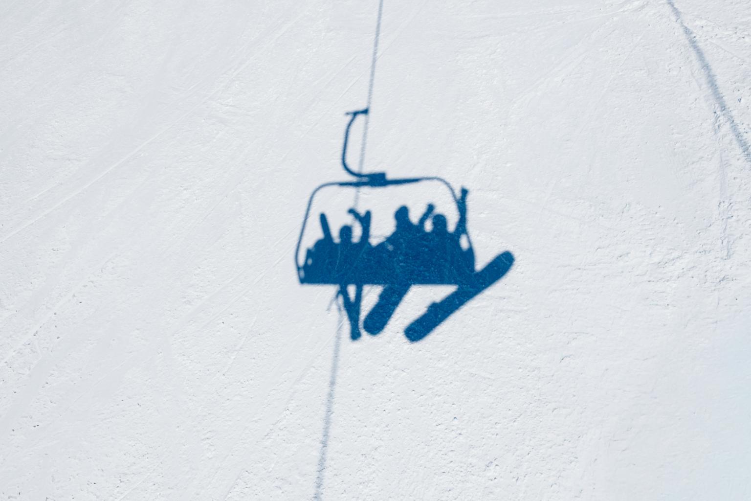 Shadow in the snow of skiers and snowboarders on a chairlift above and cheering