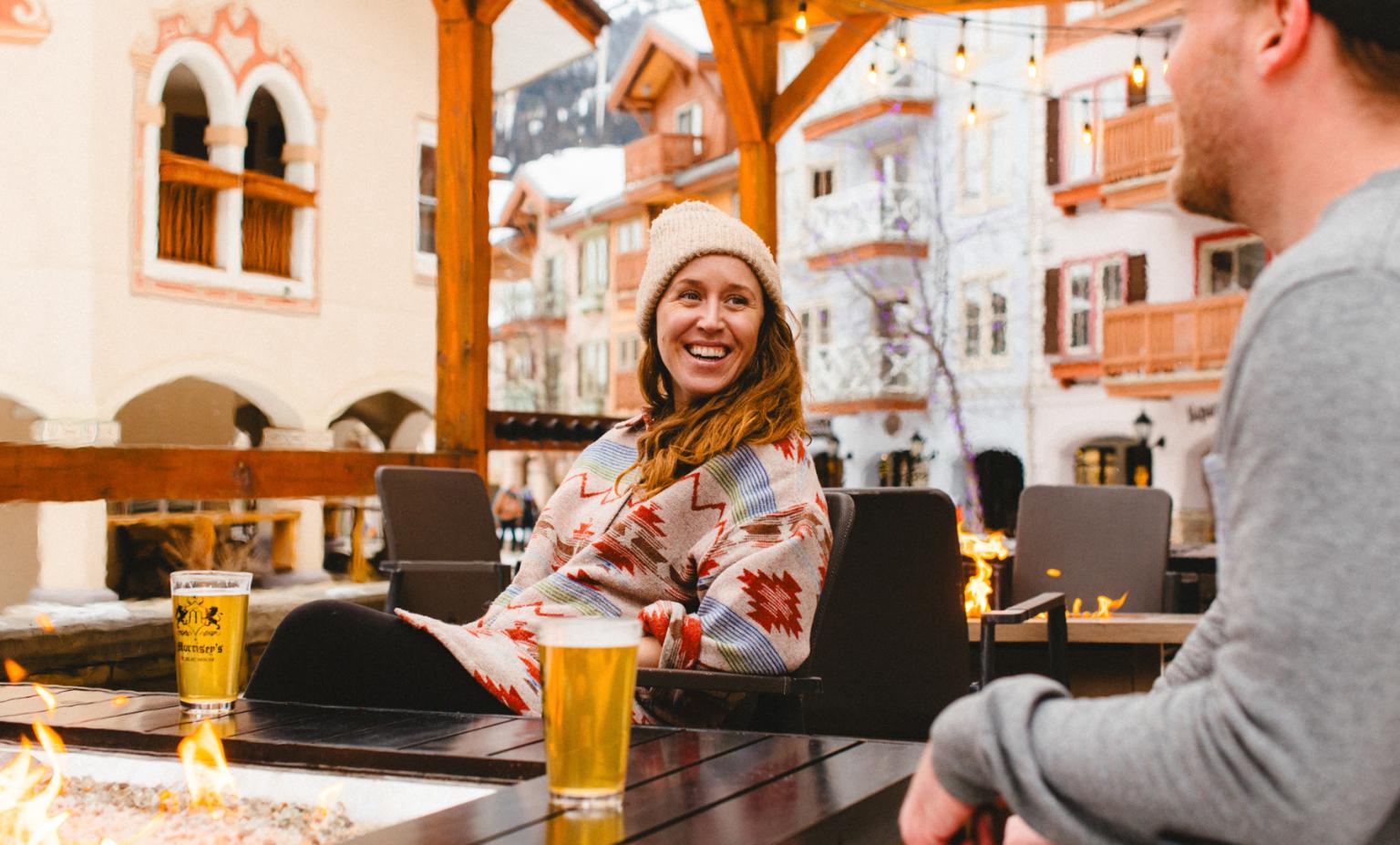 Smiling woman looking at man in an outdoor bar patio setting in sun peaks village in winter with beers on table