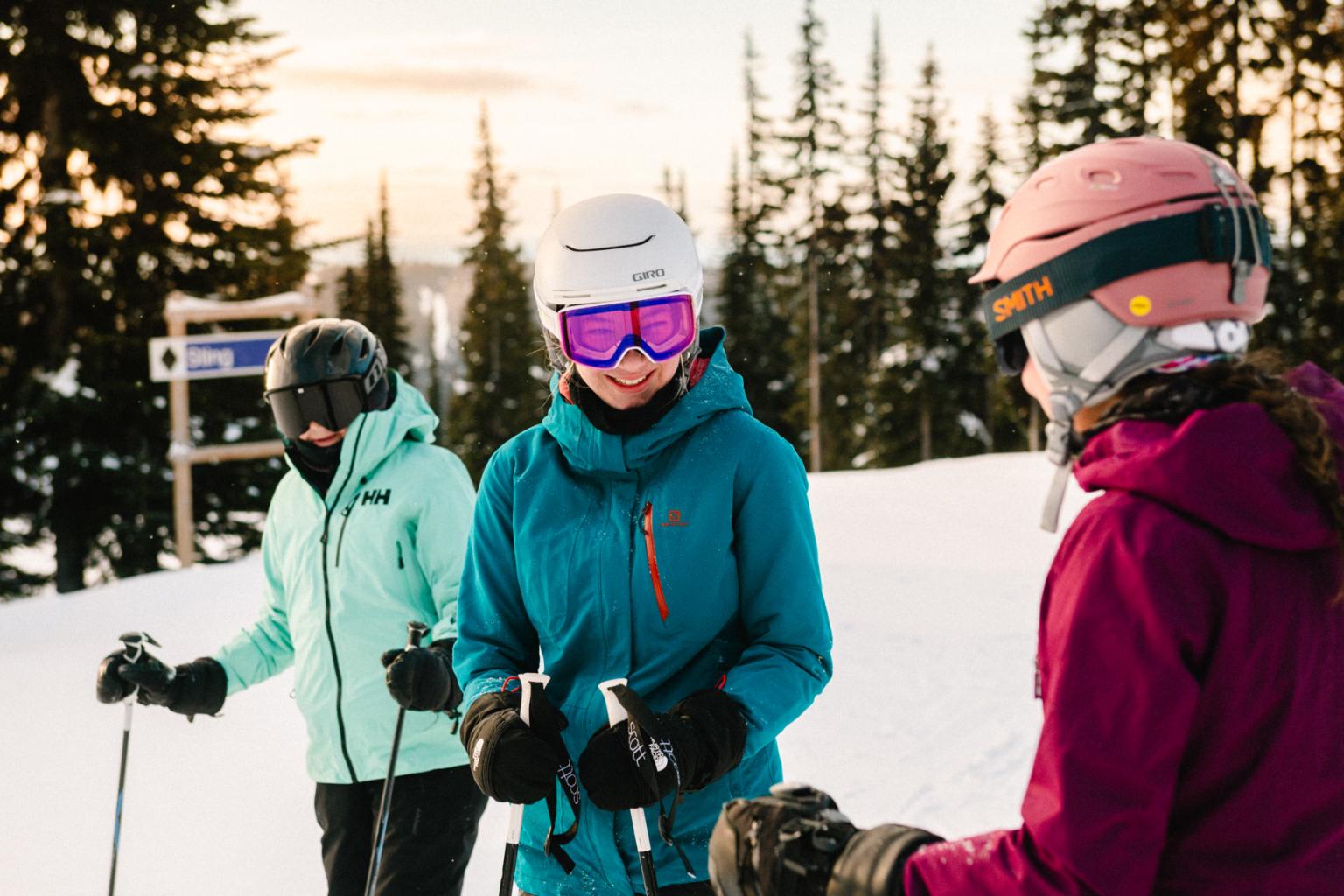 Three skiers in colorful winter gear chat on a snowy slope.