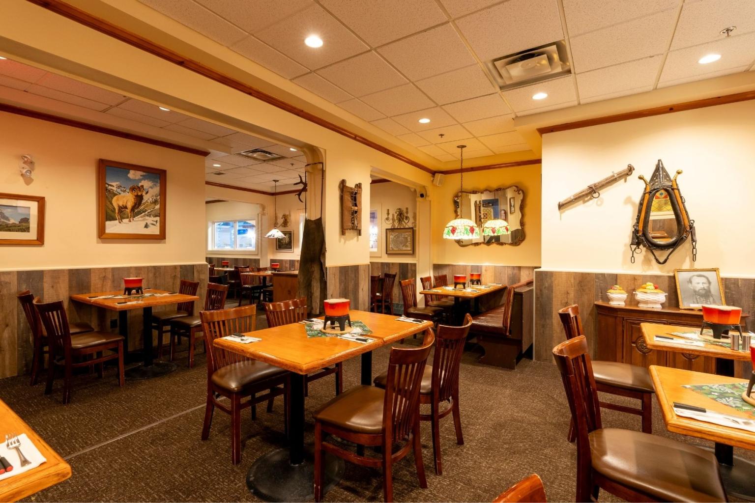 Warmly lit restaurant dining room with wooden tables, chairs, and wall art.