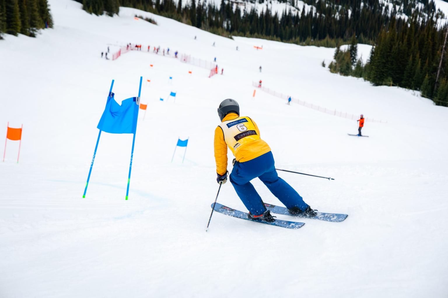 Skier in yellow jacket racing through blue slalom gates on a snowy slope.