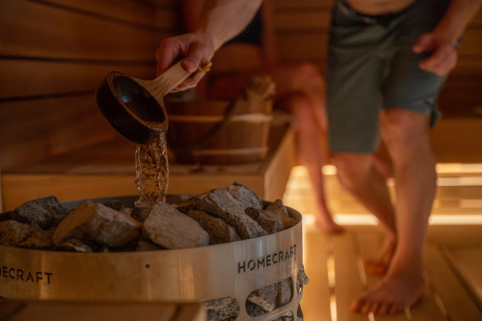Person pours water over hot stones in a wooden sauna.