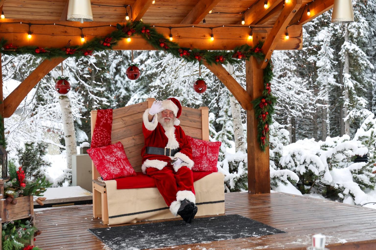 Santa Claus relaxing on a red bench in a snowy, decorated wooden gazebo.