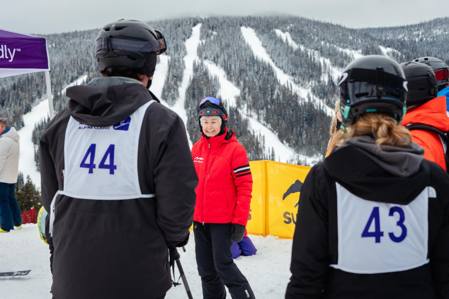 Ski event staff wearing numbered bibs 44 and 43 on a snowy mountain slope.