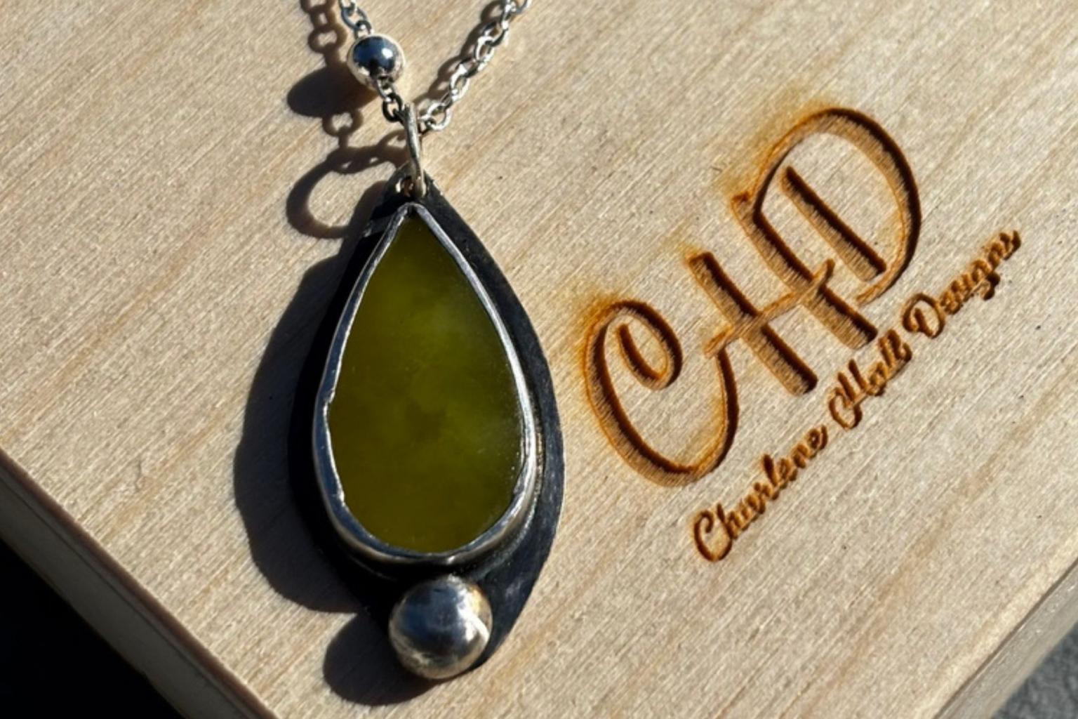 Black and olive green teardrop pendant on a wooden jewelry box.