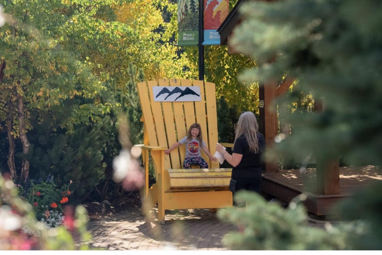 Woman standing at a yellow giant chair with a child in Sun Peaks 